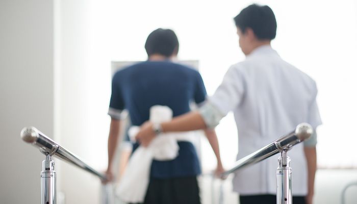 Photo of a patient using parallel bars to walk with a physical therapists assistance